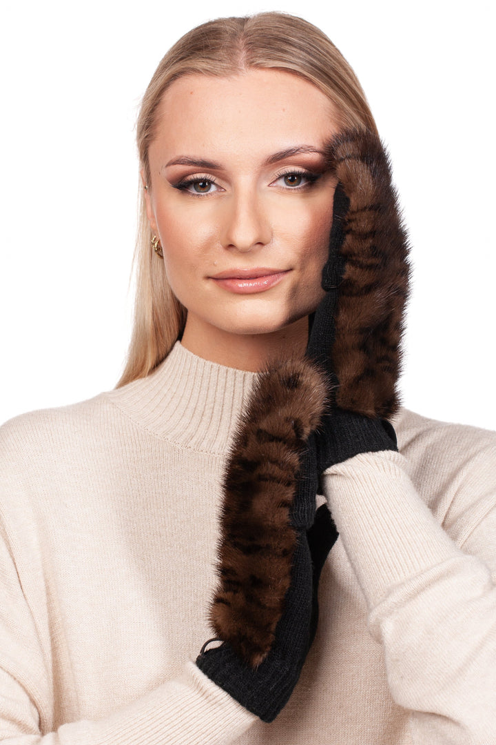 A woman with long blonde hair is wearing a cream-colored sweater and Leopard Print Mink Fur Flip Top Mittens by FurbySD, featuring ethically luxurious mink fur trims. She poses with one hand gently touching her face, displaying a gentle smile against a plain white background.