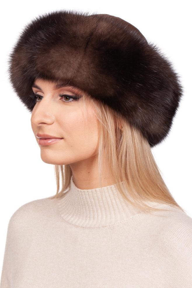 A woman models in profile against a white background, adorned in a Brown Sable Fur Roller Hat With Cashmere by FurbySD and a cream-colored sweater. Her blonde hair elegantly emerges from beneath the luxurious hat, adding an exquisite touch to her look.