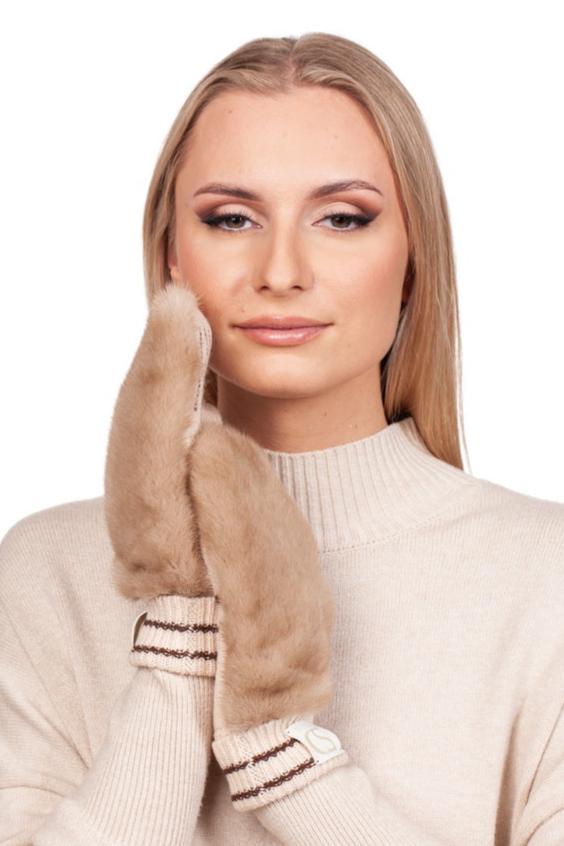 A person with long blonde hair, adorned in a light beige sweater, showcases a chic winter accessory by holding one hand to their face. They stand against a plain white backdrop, elegantly highlighting the Beige Flip Top Mink Fur Mittens by FurbySD.