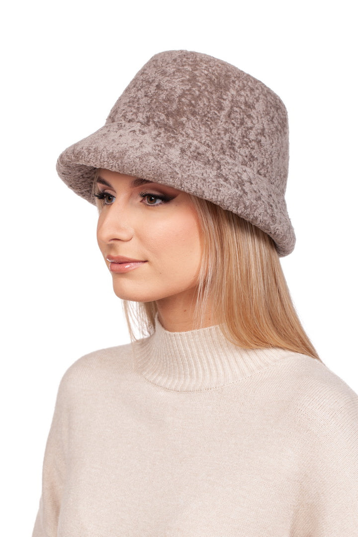 A person with long blonde hair wearing a Beige Lambskin Fur Hat With Brim by FurbySD—a luxurious winter accessory—and a white turtleneck sweater, looking to the side against a plain white background.