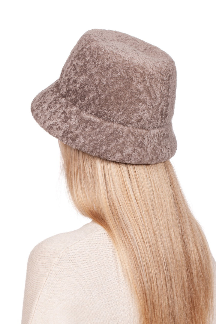 A person with long blonde hair is seen from behind, wearing a luxurious winter accessory—a FurbySD Beige Lambskin Fur Hat With Brim—and a cream-colored sweater against a plain white background.