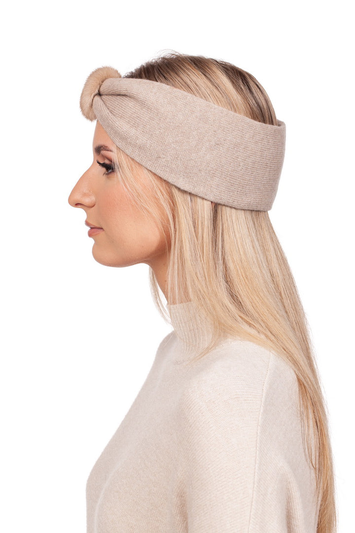 A woman with long blonde hair is wearing the luxurious Beige Mink Fur And Cashmere Headband by FurbySD, featuring a knot detail at the front. She is dressed in a matching cream sweater and is shown in profile against a plain white background, exuding an effortless elegance perfect for winter.