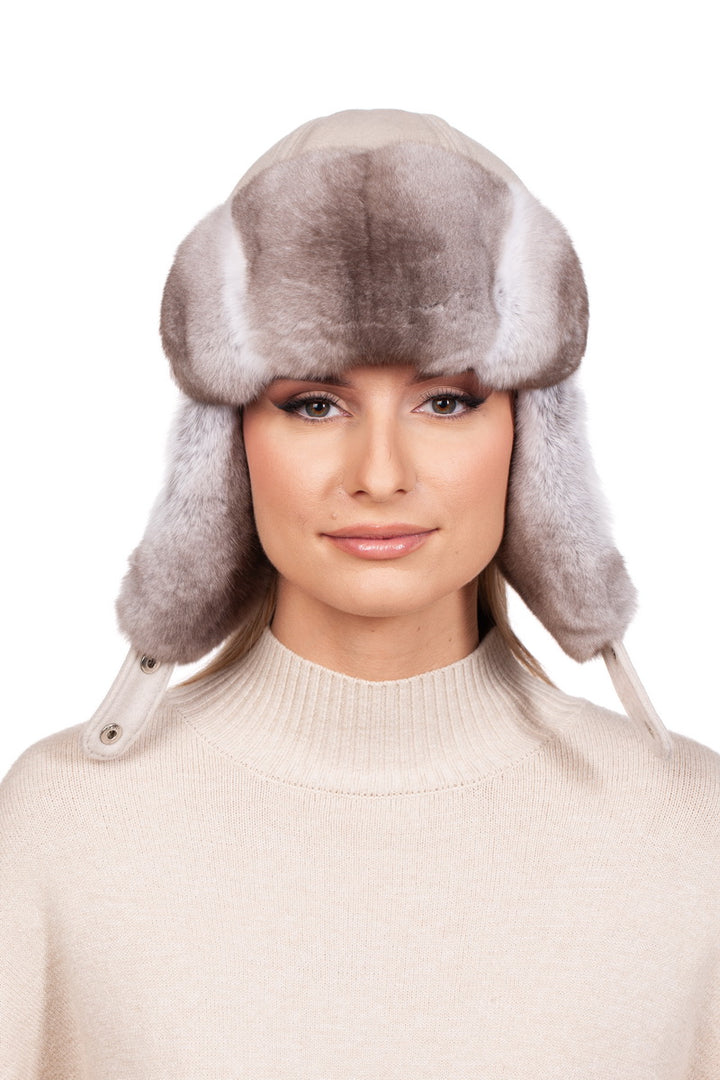 A woman dressed in a cream white turtleneck sweater, complemented by a beige chinchilla fur ushanka hat with earflaps.