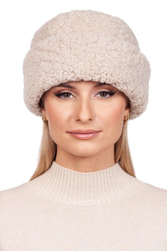 A person wearing the Beige Curly Shearling Hat and Mittens Set from FurbySD, along with a matching sweater, poses against a white background. The cozy hat, featuring its textured curly shearling fur, exemplifies perfect winter accessories style.