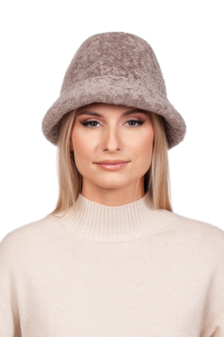 A person is wearing a Beige Lambskin Fur Hat With Brim by FurbySD, paired with a beige knit sweater, gazing directly at the camera with a neutral expression against a plain white background.