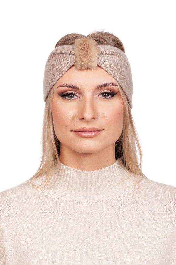 A person with long hair is wearing a FurbySD Beige Mink Fur And Cashmere Headband, featuring a front knot and fluffy detail, complemented by a matching turtleneck sweater. The luxurious winter accessory elegantly contrasts against the white background.