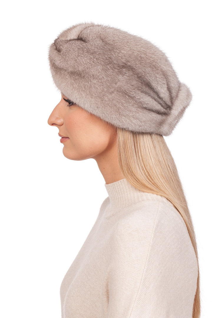 A person with long blonde hair sports an elegant winter accessory by wearing a light brown fur beret and a beige sweater. The look is completed with the Twisted Beige Mink Fur Headband from FurbySD, seen stylishly in profile against a white background.