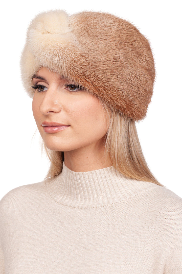 A woman with long blonde hair wears a beige turtleneck sweater and a luxurious winter accessory—a Two-Tone Beige Mink Fur Headband by FurbySD. As she gazes off to the side with a neutral expression, the genuine mink fur adds an air of elegance against the plain white background.