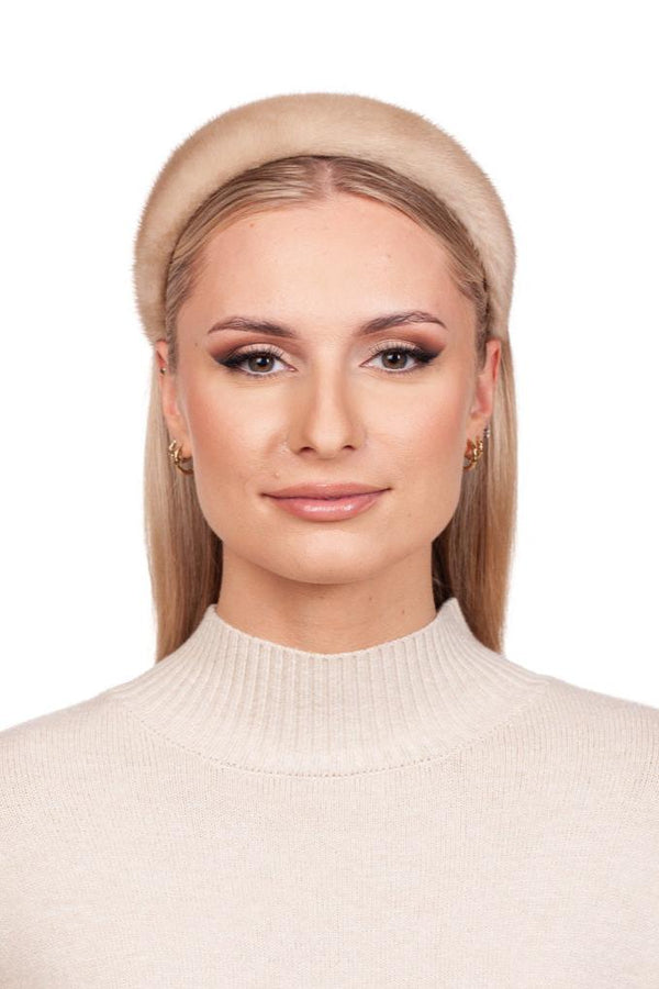 A person with long, straight hair wears a FurbySD Beige Palomino Mink Fur Headband and a cream-colored turtleneck sweater. The gold hoop earrings enhance their subtle makeup as they smile slightly against a plain white background.