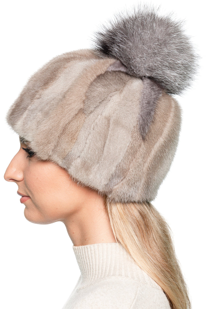 Side profile of handmade beige mink fur beanie with silver fox pom pom. Model shows the structured patchwork fur design with soft natural color shading.