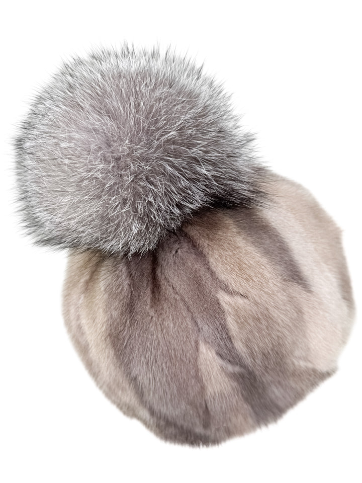 Angled view of beige patchwork mink fur hat with large silver fox pom pom. Natural mink fur pieces form a striped pattern in warm beige and soft grey tones.