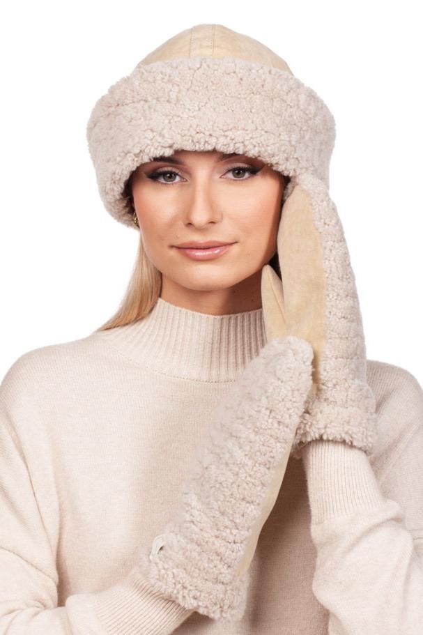 A person wears the Beige Shearling Fur Hat and Mittens Set by FurbySD, paired with a matching sweater. Sporting long blonde hair and a neutral expression, they hold the shearling mittens near their face against a white background—an elegant nod to winter fashion accessories.