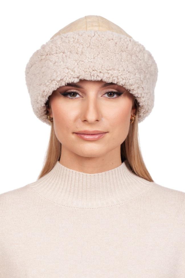 A person wearing a luxurious FurbySD Beige Shearling Fur Roller Hat and a matching turtleneck sweater stands against a white background. Their long, straight hair and subtle makeup complete the chic winter look.