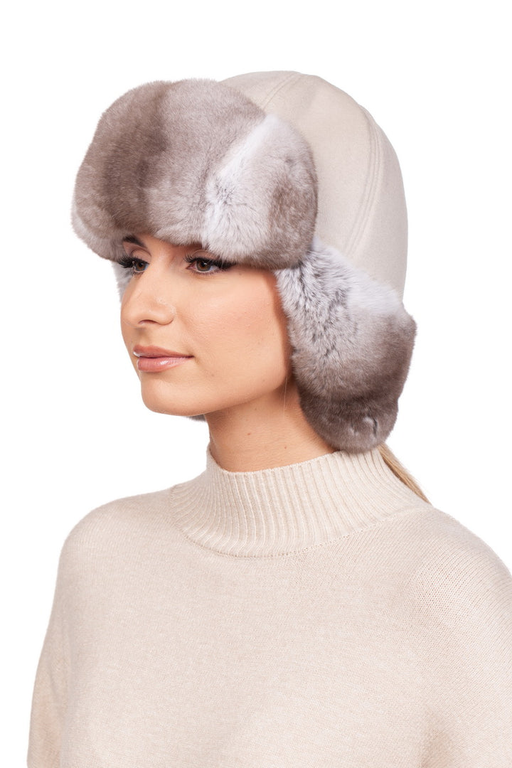 A woman in a cream white turtleneck sweater and a beige chinchilla fur trapper hat with earflaps.