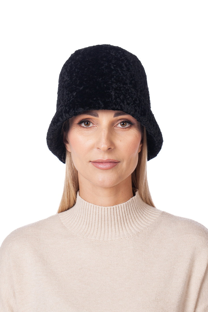 A person with long blonde hair is wearing the FurbySD Black Astrakhan Fur Hat and a beige turtleneck sweater. They are facing forward against a white background, epitomizing luxury fashion with their effortlessly chic look.