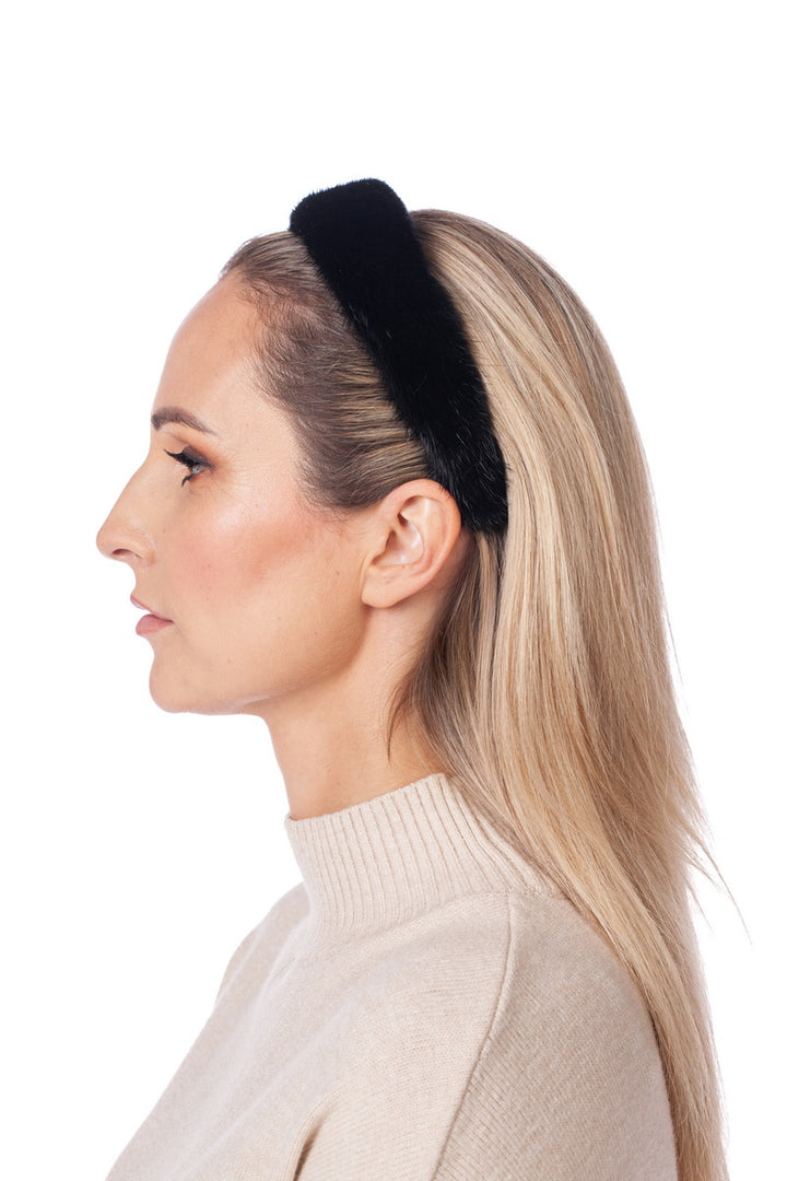 A person with long blonde hair is shown in a profile view against a white background. They are wearing the luxurious Black Mink Fur Headband by FurbySD and a beige turtleneck sweater, exuding elegance and sophistication.