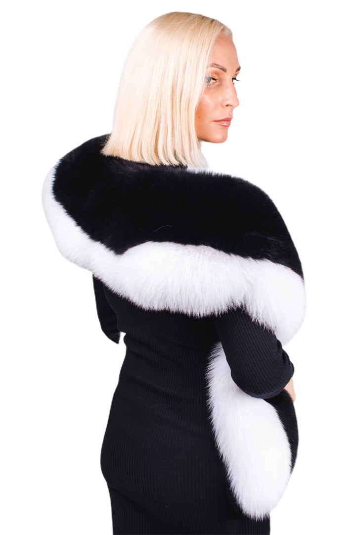 A person with blonde hair donning a black ensemble is captured from behind, elegantly wrapped in the luxurious "Black And White Fox Fur Stole" by FurbySD. The white fox fur prominently frames the black portion, creating a striking contrast against the white background that showcases this exquisite luxury fur accessory.