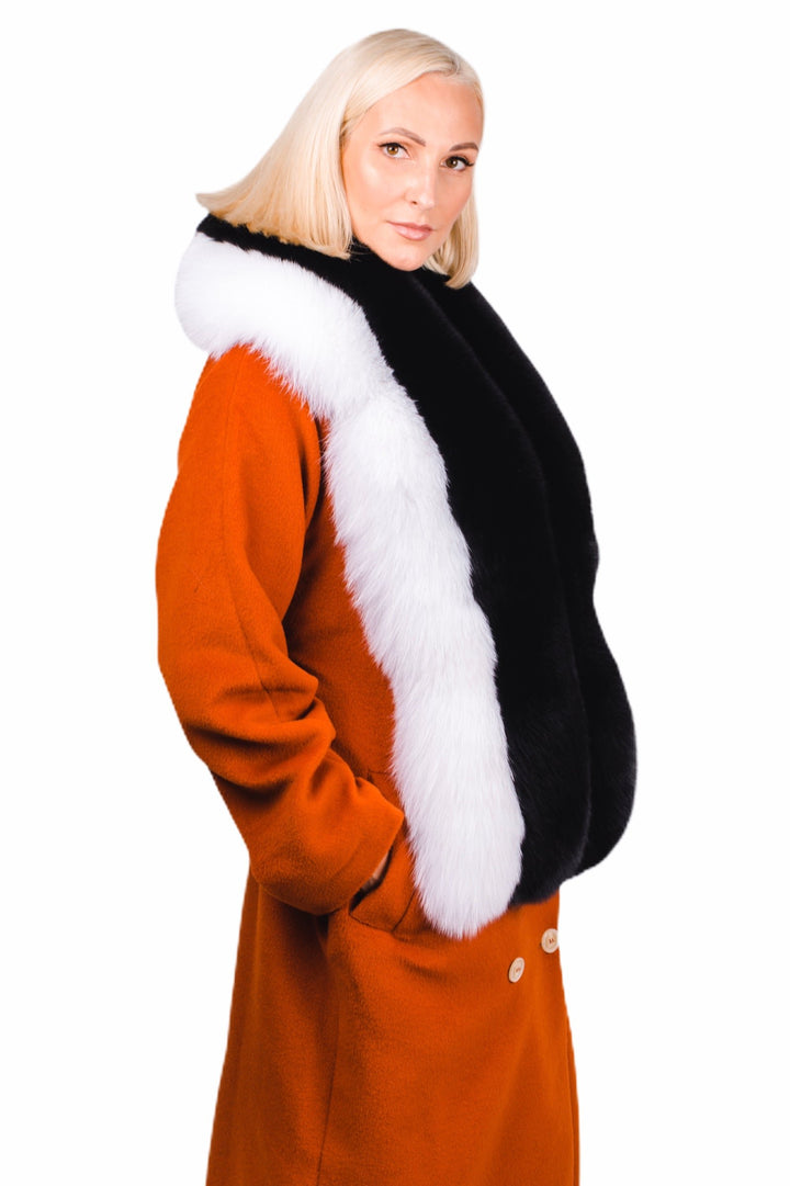 A person with short blonde hair wears an orange coat, elegantly accessorized with the luxurious Black And White Fox Fur Stole by FurbySD, their hands resting casually in their pockets. The backdrop is a simple white.