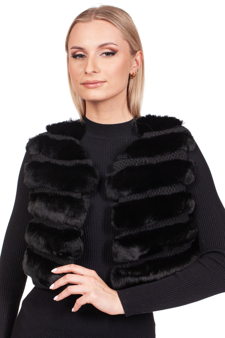 A person poses elegantly against a white background, wearing the luxurious Black Chinchilla Fur Vest With Wool from FurbySD over a black long-sleeve top. Their hand rests on their hip, framing their straight, light-colored hair with refined sophistication.