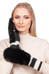 A person with long blonde hair wearing a beige sweater poses with one hand near their face, showcasing FurbySD's Black Flip Top Mink Fur Mittens. These mittens feature white stripes on the cuffs and have a plush, luxurious texture that contrasts beautifully with the smooth sweater.