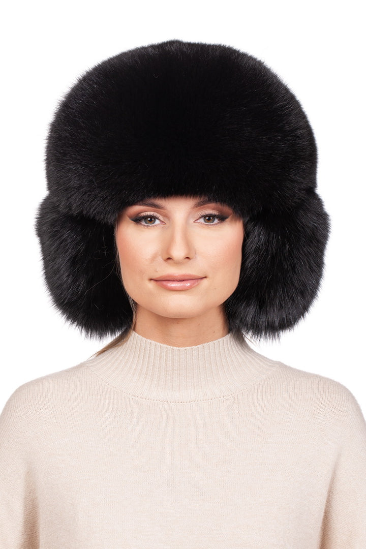 The woman wears a Black Fox Fur Ushanka Trapper Hat by FurbySD and a beige turtleneck sweater, smiling softly against a white background.