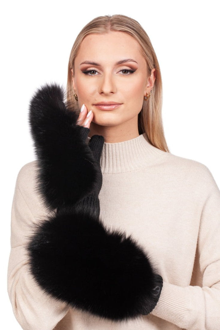 A woman with long blonde hair is wearing a beige sweater and elegant Black Fox Fur Flip Top Mittens by FurbySD. She has a neutral expression, her left hand gently touching her face against a white background.