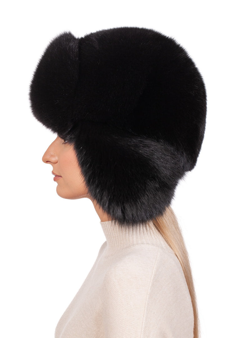 A profile of a person wearing a large, Black Fox Fur Ushanka Trapper Hat by FurbySD. The individual has long, blonde hair and is dressed in a light-colored, high-neck sweater against a plain white background.