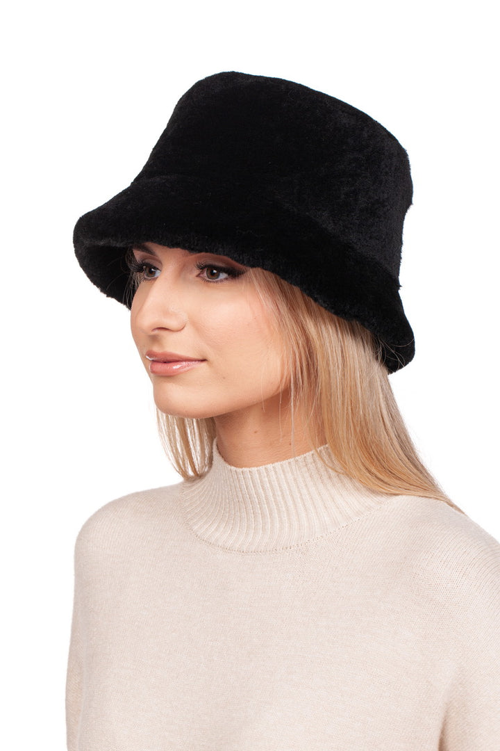 A person wearing a Black Mouton Lambskin Bucket Hat by FurbySD and a beige turtleneck sweater, looking to the side against a plain white background.