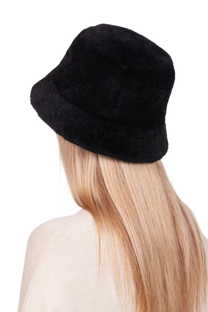 A person with long, blonde hair is seen from behind wearing the FurbySD's Black Mouton Lambskin Bucket Hat paired with a beige sweater.