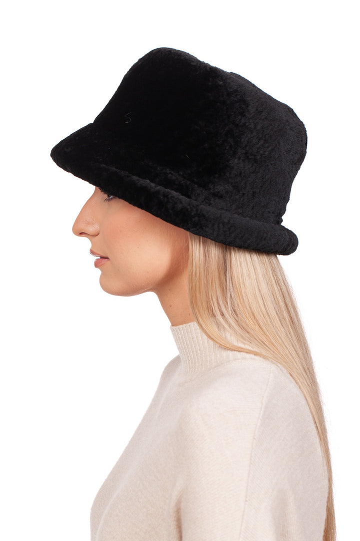 A person with long blonde hair is shown in profile against a white background, wearing the FurbySD Black Sheepskin Hat With a Brim and a cream-colored high-neck sweater. This ensemble embodies the perfect winter accessory for cold days.