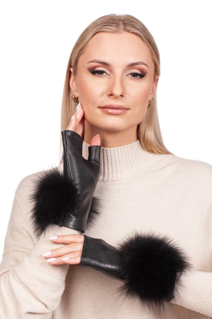 A person with long blonde hair wears a cream sweater and luxurious Black Leather Fingerless Wristlet Gloves with Fox Fur by FurbySD, handmade in Italy. Their expression is neutral as they pose gracefully, their hand near their face against a plain white background.