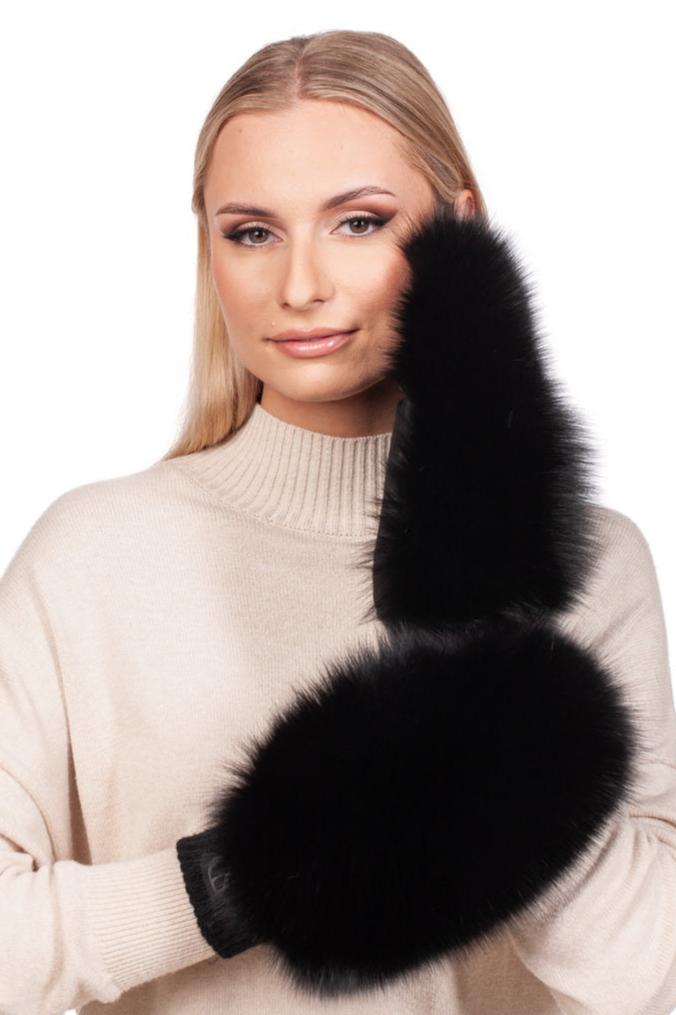 A woman in a beige turtleneck sweater holds FurbySD Black Fox Fur And Leather Mittens. Her straight, blonde hair is parted in the middle, and she poses with a neutral expression against a white background.