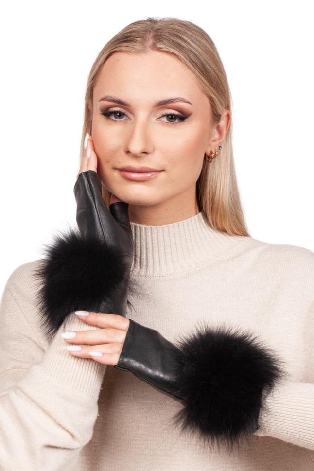 A woman with blonde hair wearing a beige turtleneck sweater smiles, showcasing the FurbySD Black Leather Fingerless Wristlet Gloves with luxurious fox fur cuffs. Handmade in Italy, she gently touches her cheek, proudly highlighting these exquisite gloves.