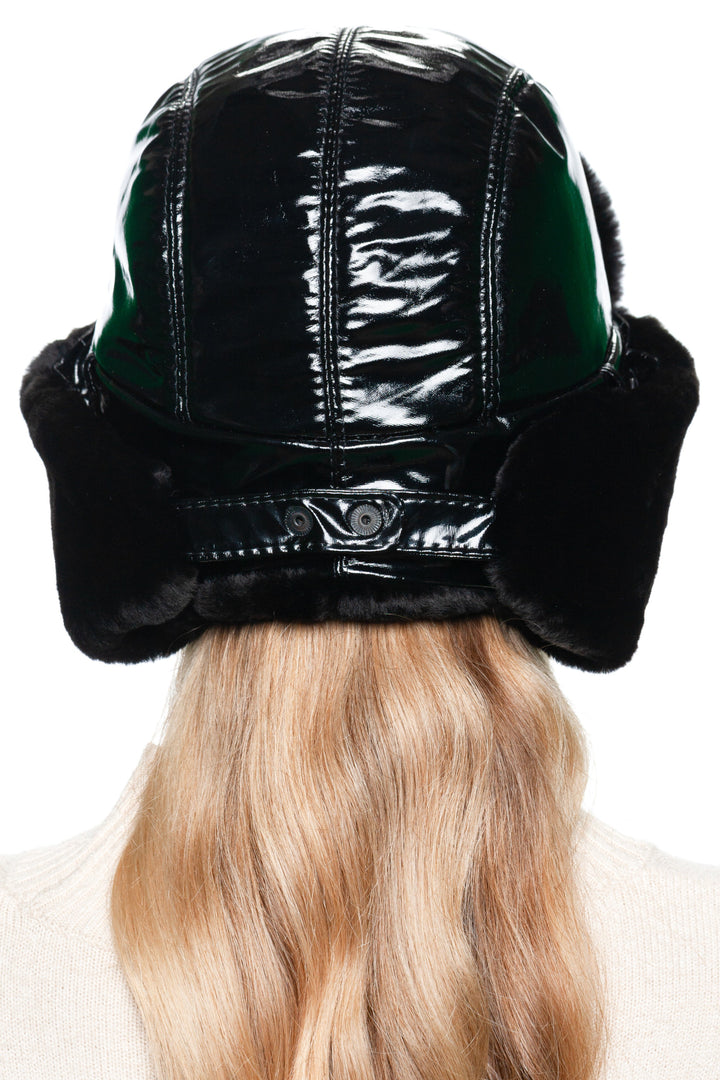 Woman wearing Black Leather and Fur Earflap Hat with chin strap down, luxury winter bomber hat with glossy leather and warm shearling fur.