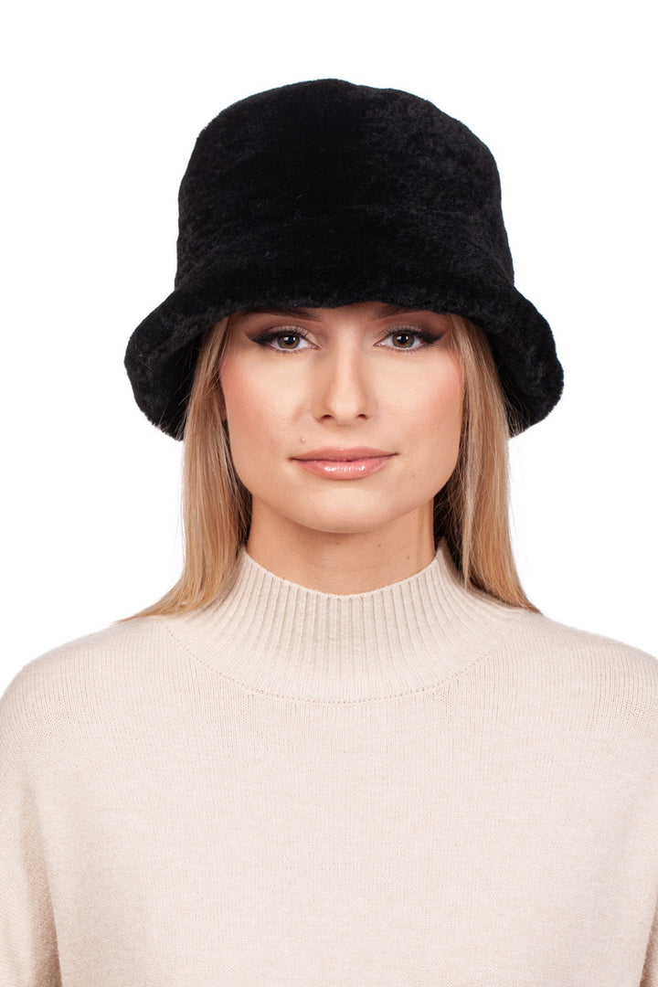 A woman wearing a FurbySD Black Mouton Lambskin Bucket Hat and a beige turtleneck sweater smiles slightly against a white background.