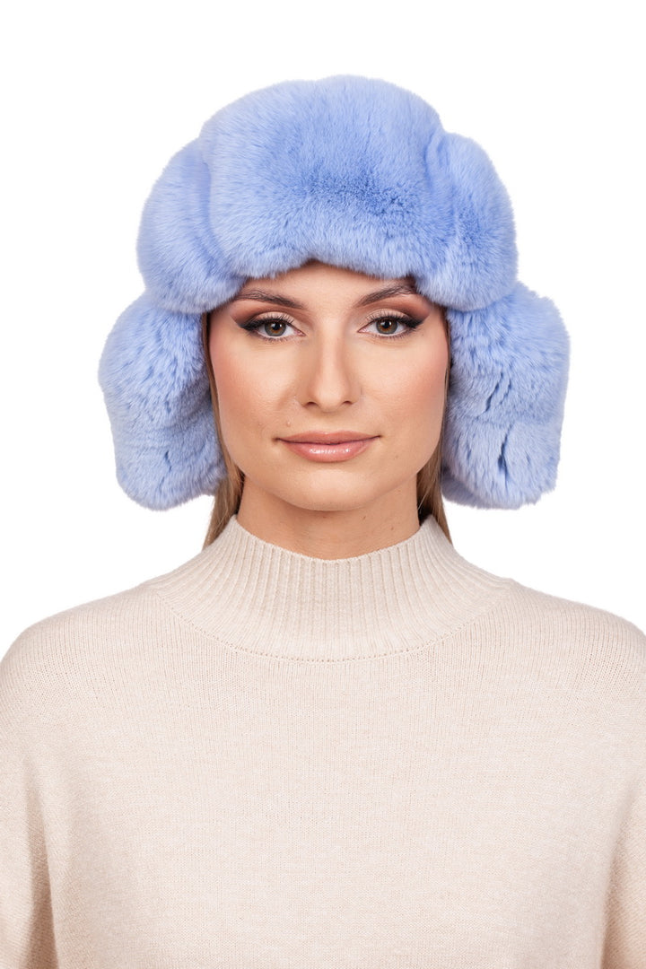 A person wearing a light blue Blue Chinchilla Fur Ushanka Hat by FurbySD with ear flaps and a beige turtleneck sweater. The background is plain white.