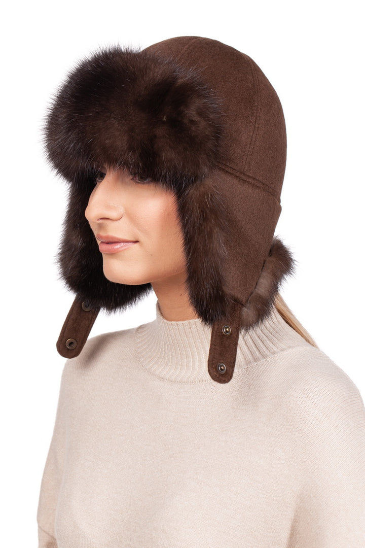 A person wearing a FurbySD Brown Barguzin Sable Fur Ushanka Hat with earflaps, paired with a beige sweater, stands against a plain white background.