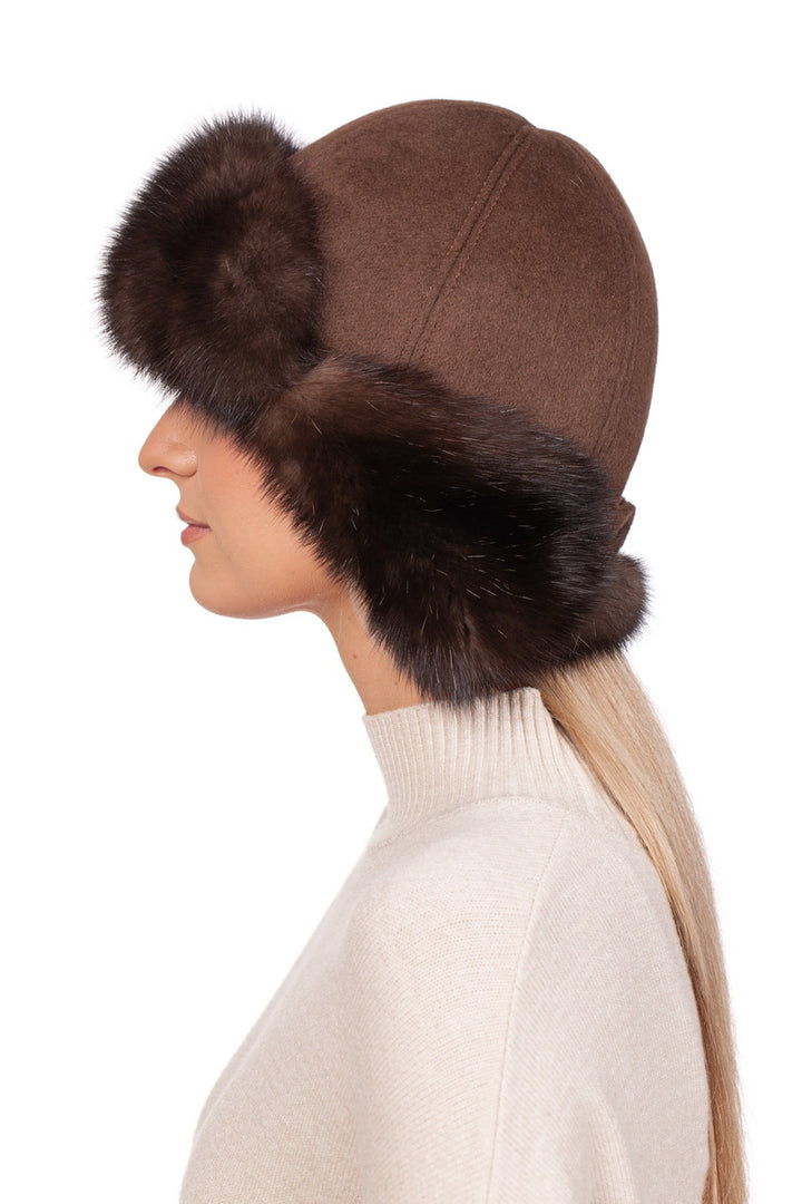 A person models to the left, wearing a sophisticated Brown Barguzin Sable Fur Ushanka Hat by FurbySD, featuring distinctive fur edges that emphasize its design. Complementing this winter accessory is a cream-colored turtleneck sweater, all set against a plain white backdrop.