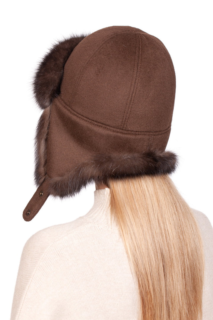 A person with long blonde hair is seen from behind, wearing the Brown Barguzin Sable Fur Ushanka Hat by FurbySD. The hat showcases ear flaps that cover the ears and includes a short strap hanging down, harmoniously complementing their light-colored top.