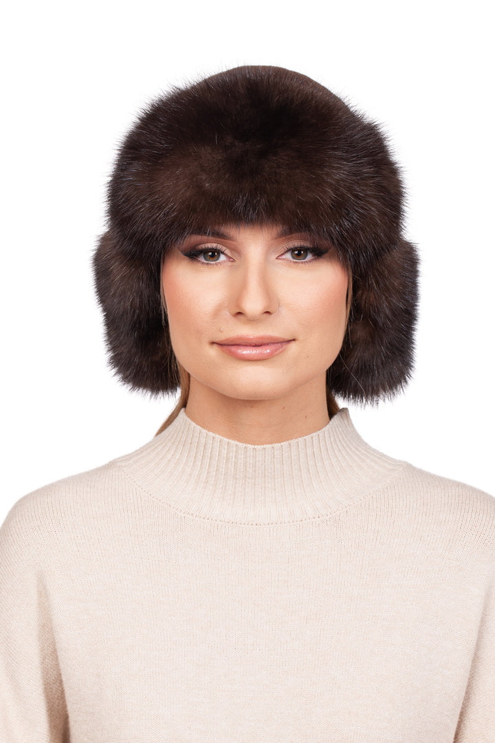 A person wearing a beige turtleneck sweater and an oversized, fluffy Brown Barguzin Sable Fur Ushanka Hat with ear flaps from FurbySD. This stylish winter accessory exudes warmth against the plain white background.