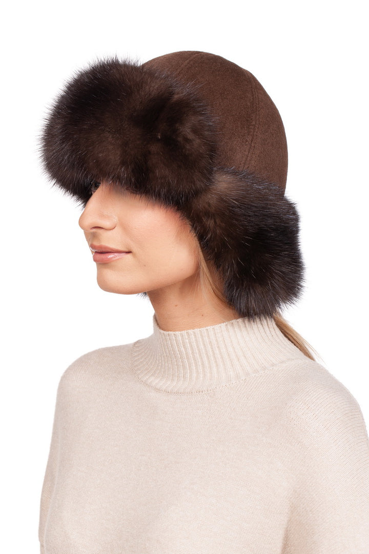 The individual is wearing a Brown Barguzin Sable Fur Ushanka Hat by FurbySD, featuring luxurious dark sable fur trim around the brim. They are paired with a light-colored turtleneck sweater, all set against a white backdrop that accentuates this sophisticated winter accessory.