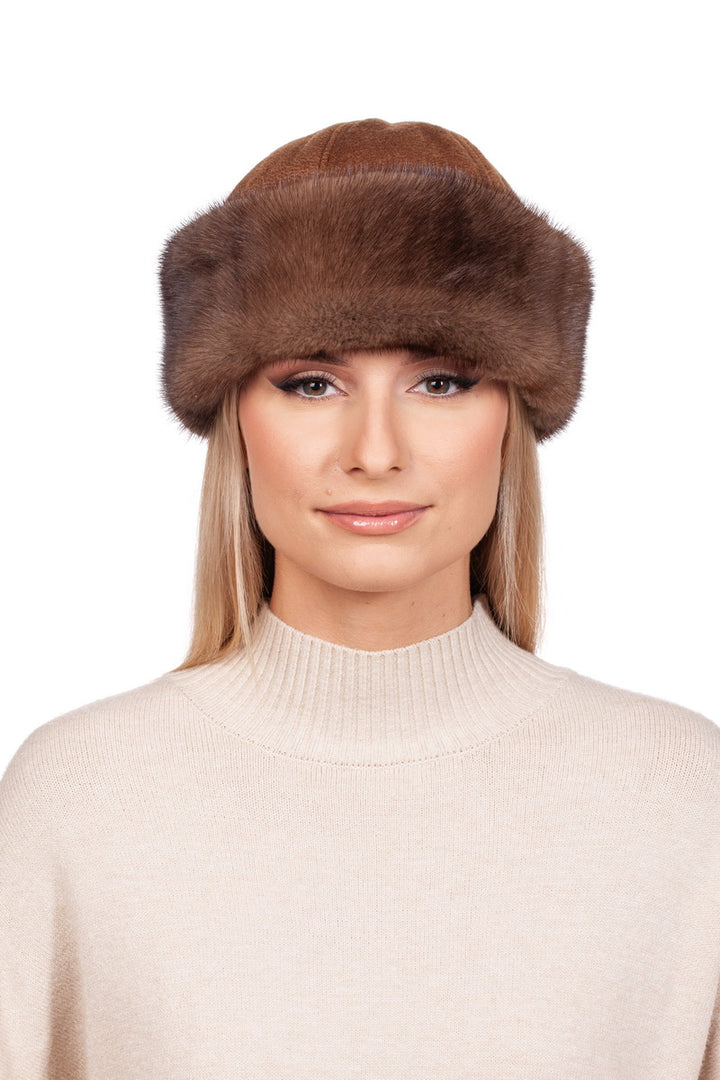 A woman with long blonde hair is sporting a luxurious FurbySD Brown Cashmere and Mink Fur Roller Hat, handcrafted in Lithuania, along with a beige turtleneck sweater. She gazes directly at the camera with a neutral expression against a plain white backdrop.