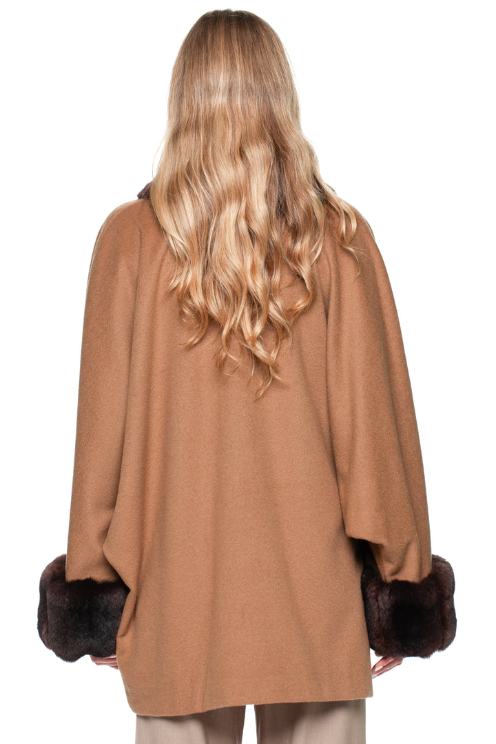 A woman wearing a brown cashmere coat with dark brown chinchilla fur cuffs on a white background.