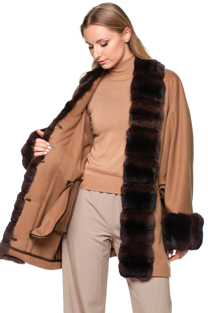 Blond woman wearing a brown cashmere coat with dark brown chinchilla fur trim on a white background.