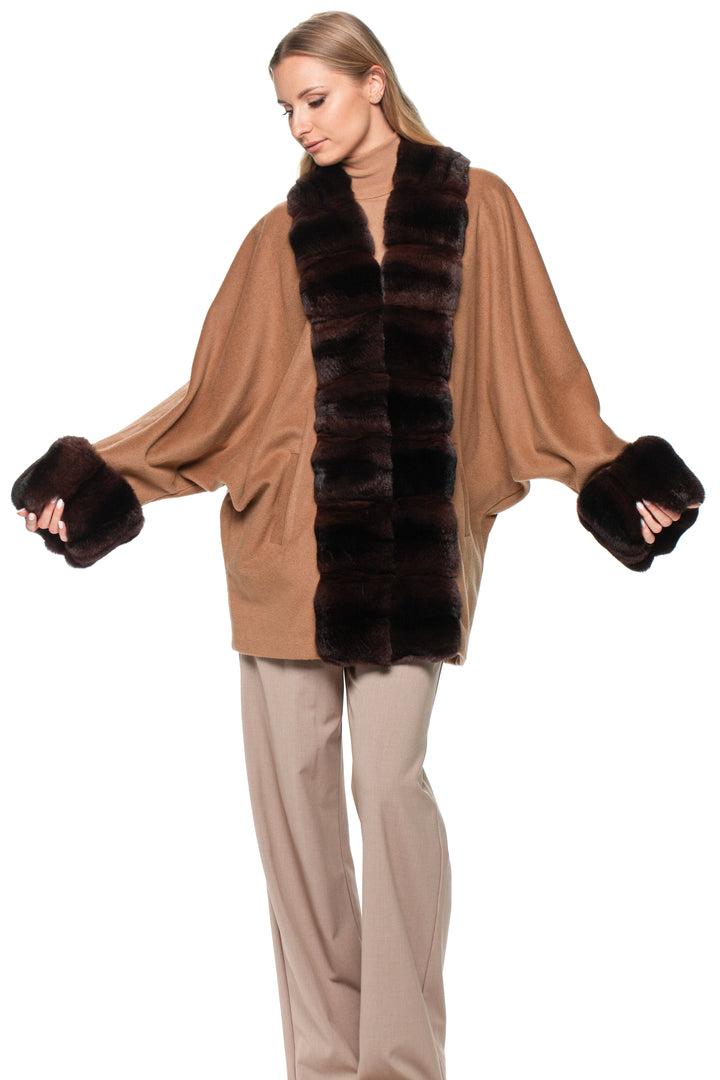 Woman wearing a beige poncho with brown chinchilla fur trim and matching pants on a white background