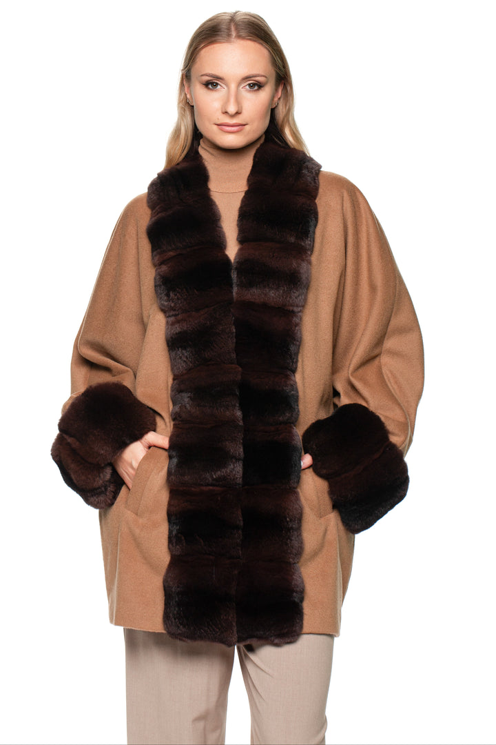 Woman wearing a tan cashmere coat with a dark brown chinchilla fur trim on a white background