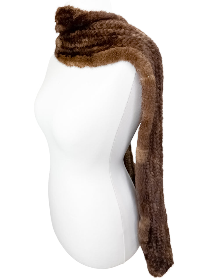 A white mannequin displays the Brown Knitted Mink Fur Scarf from FurbySD, elegantly arranged around its neck. This stylish scarf, crafted from ethically sourced fur, features a rich brown hue and a soft, plush texture that gracefully drapes down each side of the mannequin.