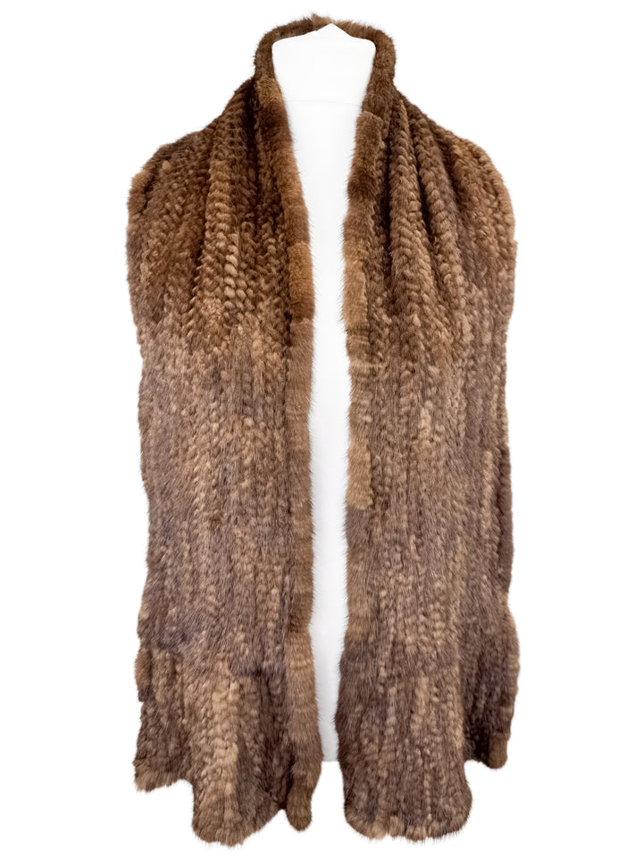 A Brown Knitted Mink Fur Scarf from FurbySD elegantly draped over a mannequin. The scarf showcases a soft, textured pattern and boasts a rich, natural appearance, crafted from ethically sourced fur.