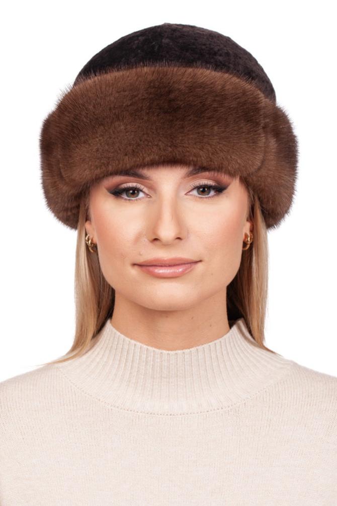 A person dons the Brown Mink And Astrakhan Fur Roller Hat by FurbySD and a cream-colored turtleneck sweater. Their long blonde hair cascades around their shoulders, complemented by gold hoop earrings as they pose against a white background, highlighting premium winter accessories.