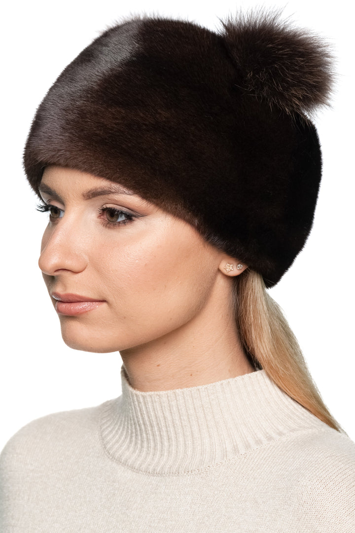 Woman wearing a brown fox fur pom-pom hat on a white background.